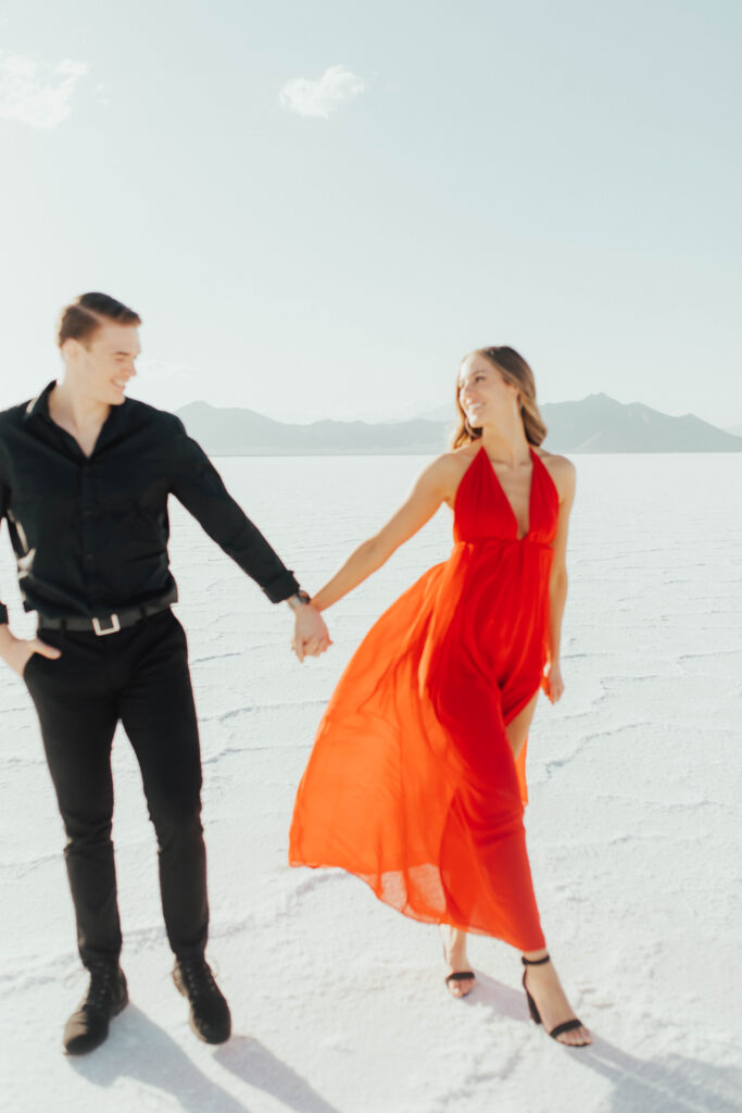 Flowing red gown caught in the wind during romantic Salt Flats engagement session, specifically has the salt flats landscape in focus instead of couple.