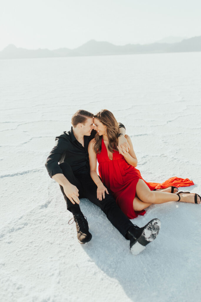 Couple sitting on the ground at the Bonneville Salt Flats, leaning forehead to forehead during their destination Salt Flats engagement session.