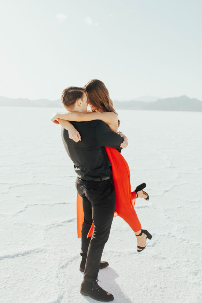 Couple embracing at Bonneville Salt Flats with bride in dramatic red dress.