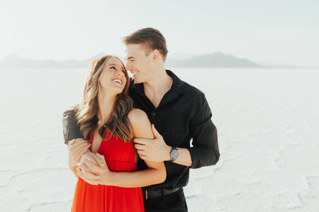 Groom holding bride close during red dress Salt Flats engagement session.