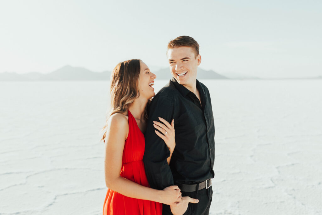 Couple laughing together during red dress destination Salt Flats engagements.