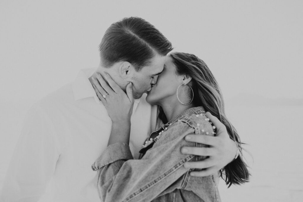 Black and White photo of bride grabbing groom's face and kissing him at Bonneville Salt Flats engagement session.