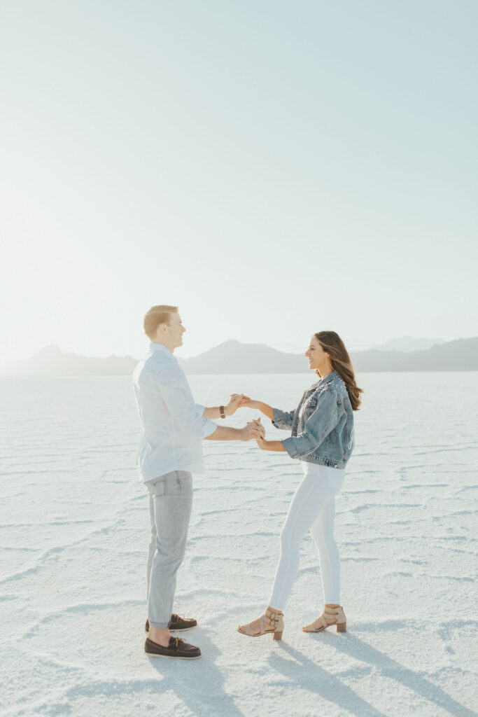 Couple holding hands and dancing during their destination Salt Flats engagements, with soft golden light on the white landscape.
