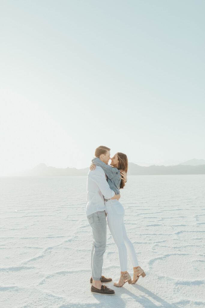 Couple embracing closely during destination Salt Flats engagements, standing in warm golden-hour light at Bonneville.