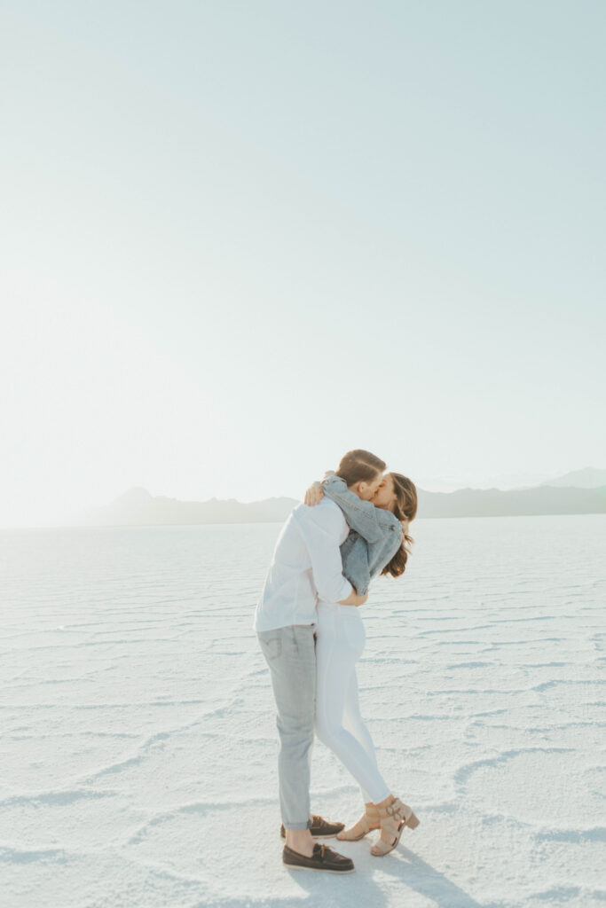 Romantic kiss during destination Salt Flats engagements, with the couple wrapped in each other as the mountains fade in the background.
