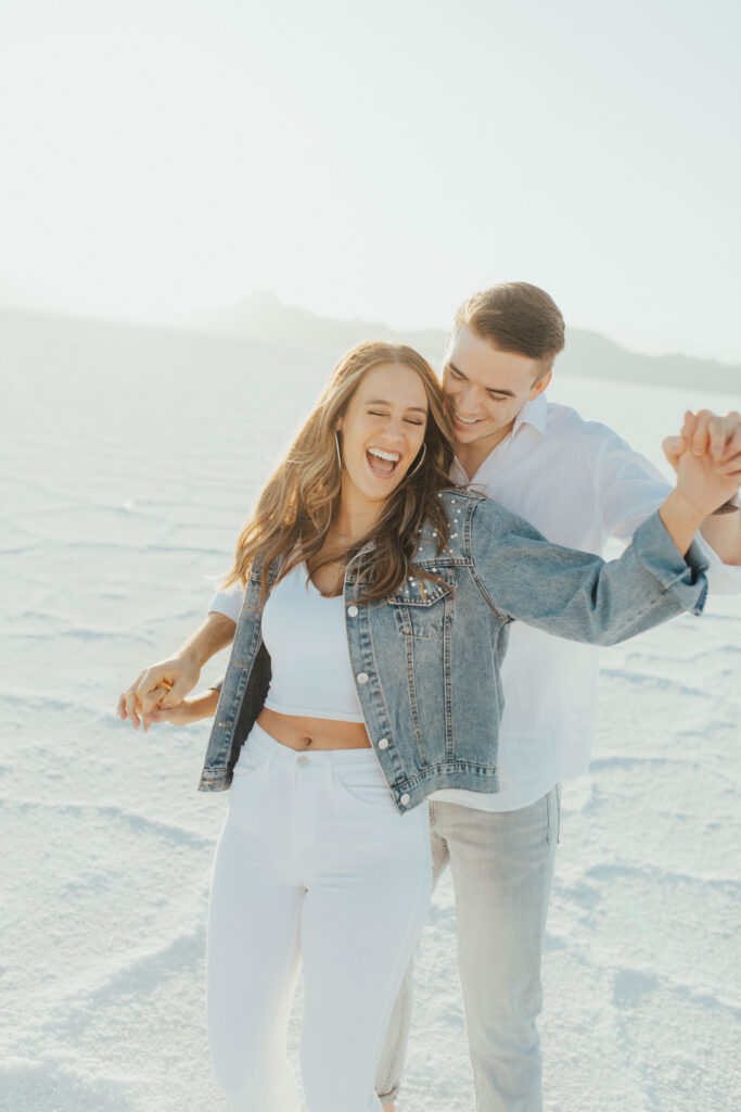 Close-up of bride laughing while groom embraces her during destination Salt Flats engagements at golden hour.