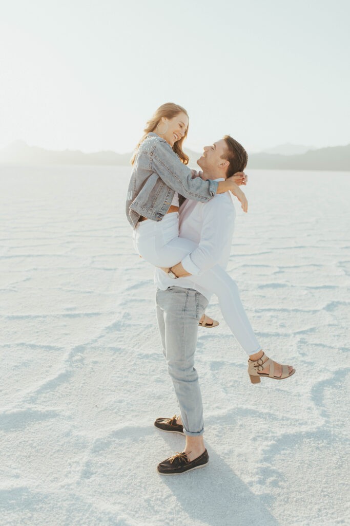 Groom lifting bride into the air during destination Salt Flats engagements, creating a joyful and romantic moment at Bonneville.