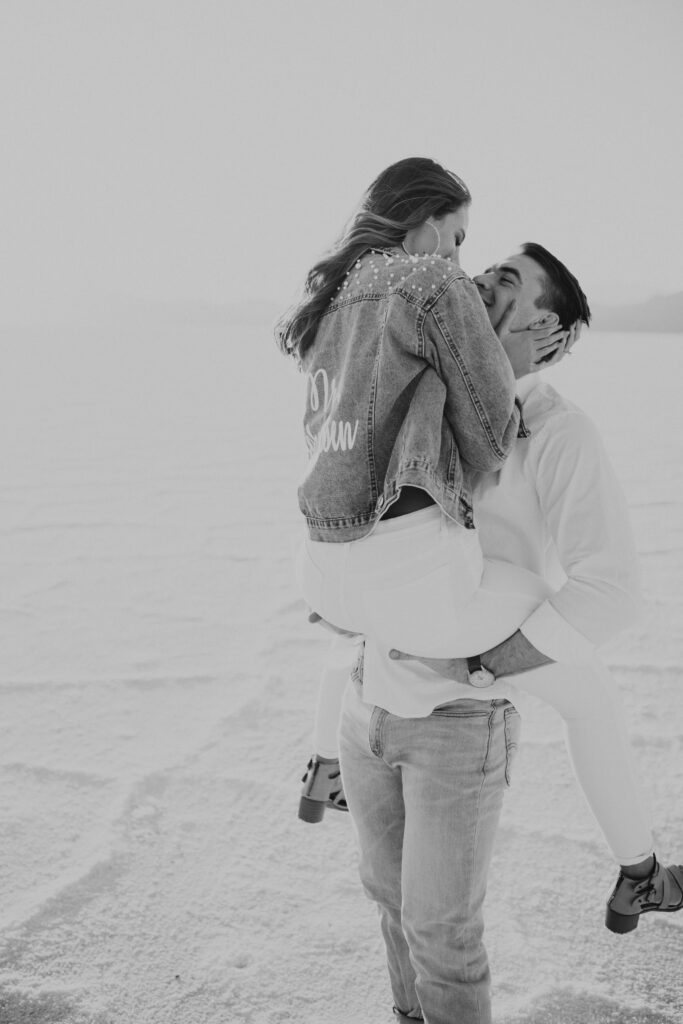 Black and White photo of bride smiling with custom jean jacket during destination Salt Flats engagements.