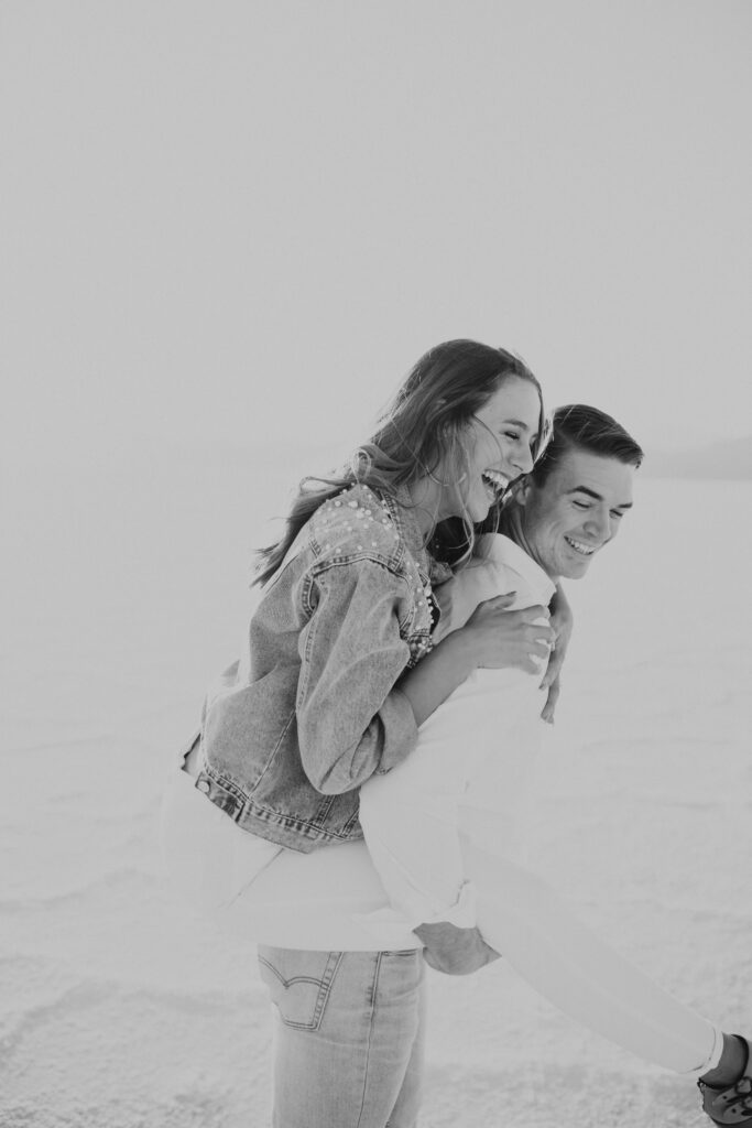 Candid black and white photo of groom giving his bride a piggy back ride.