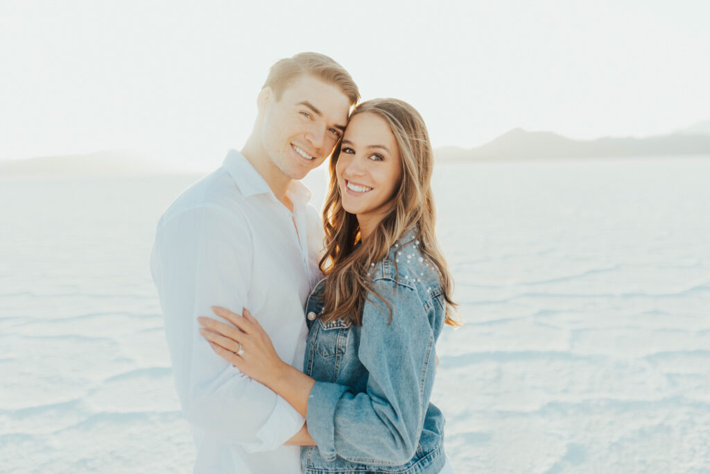 Couple smiling at the camera during their destination Salt Flats engagements, with soft golden light behind them.