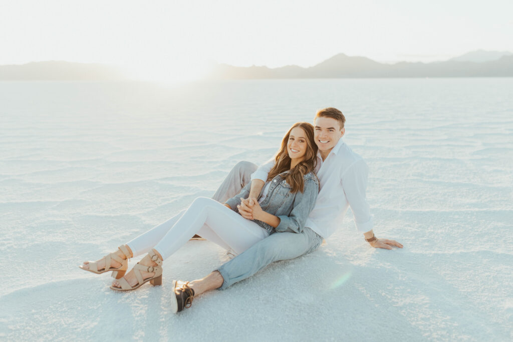Couple sitting on the white Salt Flats during destination engagements, leaning into each other as the sun sets behind the mountains.